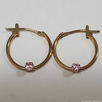 Front view of both 10K yellow gold hoop earrings with single pink cubic zirconia stones on each hoop.