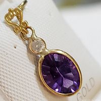Front close-up of pendant showing oval purple amethyst and round diamond in 14K yellow gold setting with intricate bail.