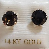 Front view of two round smokey quartz earrings set in 14K white gold prong settings displayed on white background with 14K gold marking visible.
