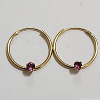 Pair of 14K yellow gold hoop earrings with pink tourmaline stones seen from above on white background.