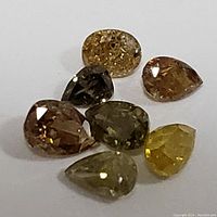 Seven assorted fancy color diamonds in various shapes and hues on white background.