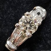 Oblique close view of ring face showing round center diamond and accent stones on both shoulders