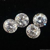 Four round cut cubic zirconia stones laid out on a dark background.