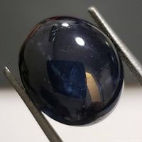 Close-up image showing the deep blue polished surface of the star sapphire gemstone held by tweezers, highlighting the star effect under light.