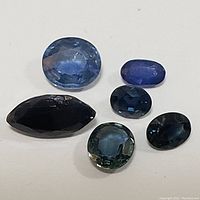 Five loose sapphire gemstones displayed on a white background showing various cuts and blue tones.
