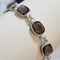 Close-up view of several faceted smokey quartz stones in sterling silver setting showing quality and details of the stones and metal work.