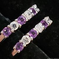 Close-up photo of one sterling silver hoop earring showing alternating round amethyst and white stones in prong settings.