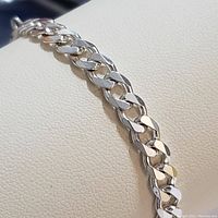 Close-up view of the sterling silver flat curb bracelet chain links resting on a cream leather surface.