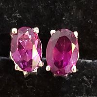 Close-up of two sterling silver earrings with oval faceted garnet gemstones set in four-prong mounts on black background.