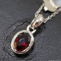 Close-up image of oval faceted garnet gemstone set in polished sterling silver pendant attached to sterling silver chain.