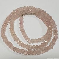 Faceted rose quartz bead necklace coiled, showing the color, shape, and clarity of beads.