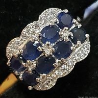 Angled top view showing eight oval blue sapphires and surrounding clear accent stones