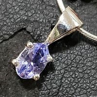 Close-up photo showing oval tanzanite gemstone in 4-prong sterling silver setting pendant, with polished bail on snake chain.
