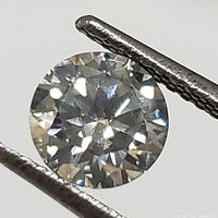 Round brilliant cut loose gemstone held by tweezers shown on white background.