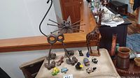 Overview of the lot including forged metal cat, wooden giraffe, and various small animal figurines on a beige surface.