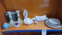 Overview of ceramic and china items including plates, candlesticks, flower figurine and pitchers.