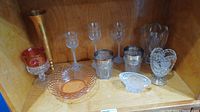 Photo showing various stemware glasses, small crystal dishes, and decorative items arranged inside a wooden shelf.