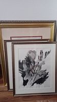 Set of three floral framed artworks leaning against a wall, including one in a gold ornate frame