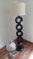 Modern black floor lamp with five circular open sections stacked vertically and white fabric shade. Floor lamp stands approximately 60 inches tall. Base and light socket visible at bottom.