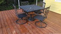 Overview photo of square black metal patio table with four swivel chairs around it, showing lattice design on table and chairs.
