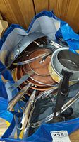 Photo showing the pots and pans inside a blue striped reusable shopping bag including a large floral patterned pot and copper non-stick pans stacked inside.