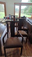 Set of six wooden dining chairs with upholstered beige seats arranged around a dining table, showing front and partial side views.