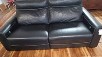 Front view of two-seat black leather power recliner sofa on wood floor