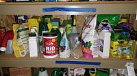 Wide view of multiple gardening products organized on shelves, including a Nu-Life Rid Moss container, various fertilizer bags, spray bottles, and other garden chemical products.