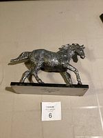 Side view of metal horse figurine mounted on a rectangular base with embossed designs.
