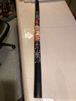 Full length view of the black didgeridoo showing painted white floral and abstract indigenous style motifs around the middle section