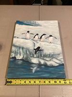 Front view of the penguin scene painting showing five penguins on icy terrain with one jumping into water, canvas edges visible.