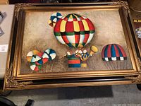 Full frontal view of the framed oil painting showing colorful geometric-patterned hot air balloons with figures inside one balloon.