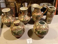 Front view of the set showing two double-handle vases, a lidded ginger jar, and a pitcher, all featuring hand-painted traditional Chinese scenes with floral and gold accents.