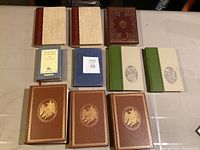 Top view of all 11 books arranged on a table showing variety of bindings and colors including leather bindings and cloth.