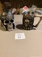 Photo showing two skull-themed collectible items, a detailed skull head decoration with helmet, and a skull mug with crossbones and bone handle.