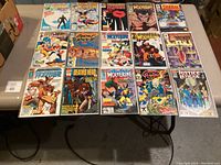 Fifteen collectible comic books arranged on a table, various titles and characters visible