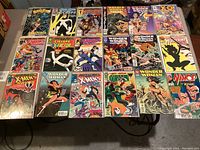 Full lot of 20 comic books arranged in 4 rows on a table, featuring Marvel and DC superhero titles including Wonder Woman, X-Men, Cyclops, X-Factor, Wolverine, and Namor.