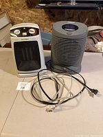 Two electric heaters on a table including a white Mainstays Max Heat heater and a gray Honeywell heater with cords.
