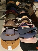 Photo showing 15 hats arranged in rows, mostly wide-brim felt and fabric hats with various colors and decorative bands.