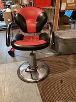 Frontal view of the barber chair showing the seat and backrest upholstery in red and black vinyl, mounted on a chrome base with footrest.