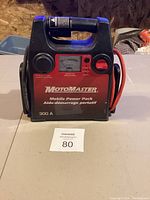 Front view of MotoMaster Mobile Power Pack showing brand, model, and battery charge meter with attached red and black cables.