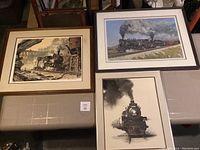 Photo showing three framed prints of steam trains in various scenes with smoke and detailed backgrounds, laid out on a surface.