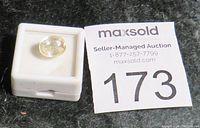 Yellow sapphire gemstone in small jewelry display box next to auction number card.