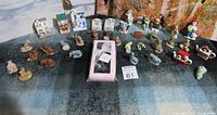 Wide shot showing assortment of about 30 assorted small figurines including animal figures, tiny houses, and other curios, all laid out on a blanket surface.