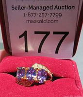 Front view of gold tone ring sized 6 with three oval purple amethyst stones and clear accent stones on curved band sides.