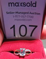Front view of the 10K gold aquamarine ring in a red velvet ring box with auction tag 107 visible