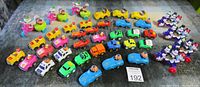 Wide shot of all vintage toy cars arranged in rows on a textured surface showing multiple colors and character drivers