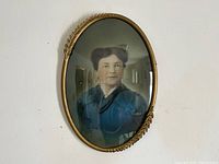 Front view of oval vintage brass frame with curved glass and portrait photograph inside showing Sarah Ellen White in blue clothing.