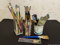 Wide view of paint brushes in various containers showing multiple sizes and types.