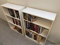 Two white bookshelves filled with assorted books placed side-by-side showing overall condition and contents